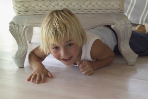 Small blonde child crawling under a living room chair