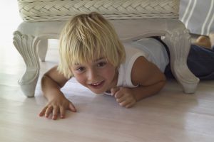 Small blonde child crawling under a living room chair